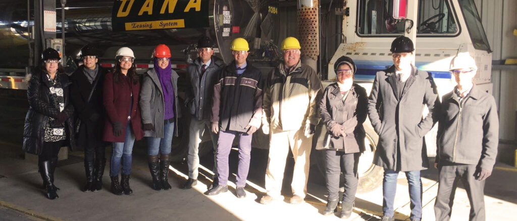 Group of individuals standing in front of truck with hard hats.